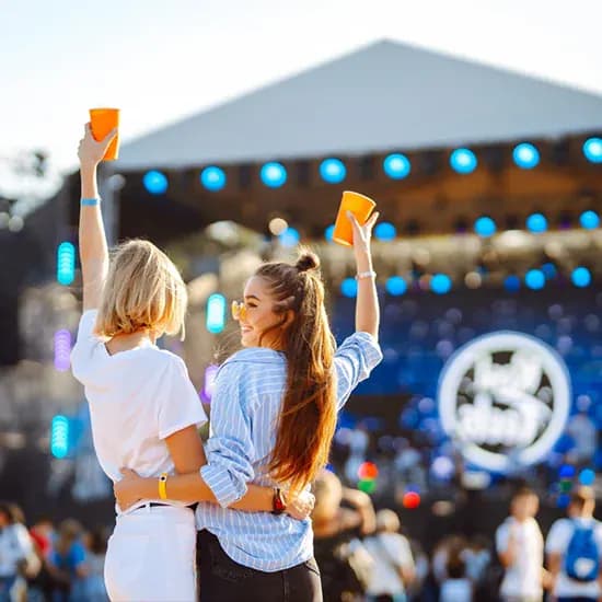 Festival crowd raising drinks in front of an outdoor stage