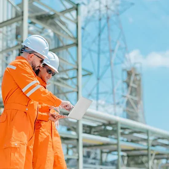 Two groundworks engineers in orange high-visibility clothing reviewing work on a laptop beside site infrastructure