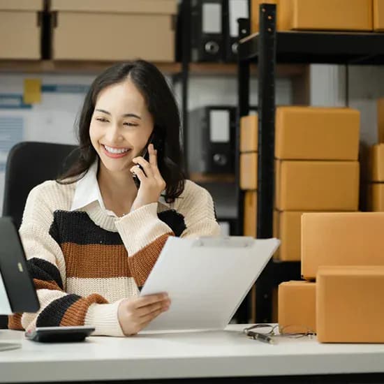Manufacturing office worker speaking on the phone while holding a clipboard beside stacked boxes